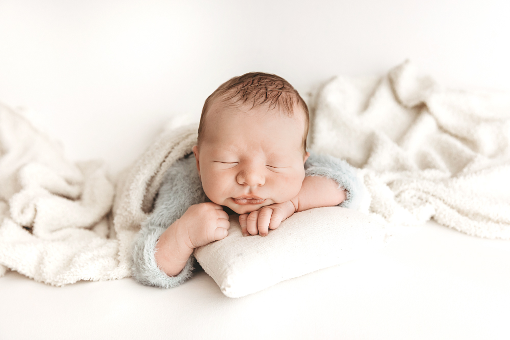 Sleeping newborn baby wrapped in soft gray blanket on cream textured backdrop by professional photographer