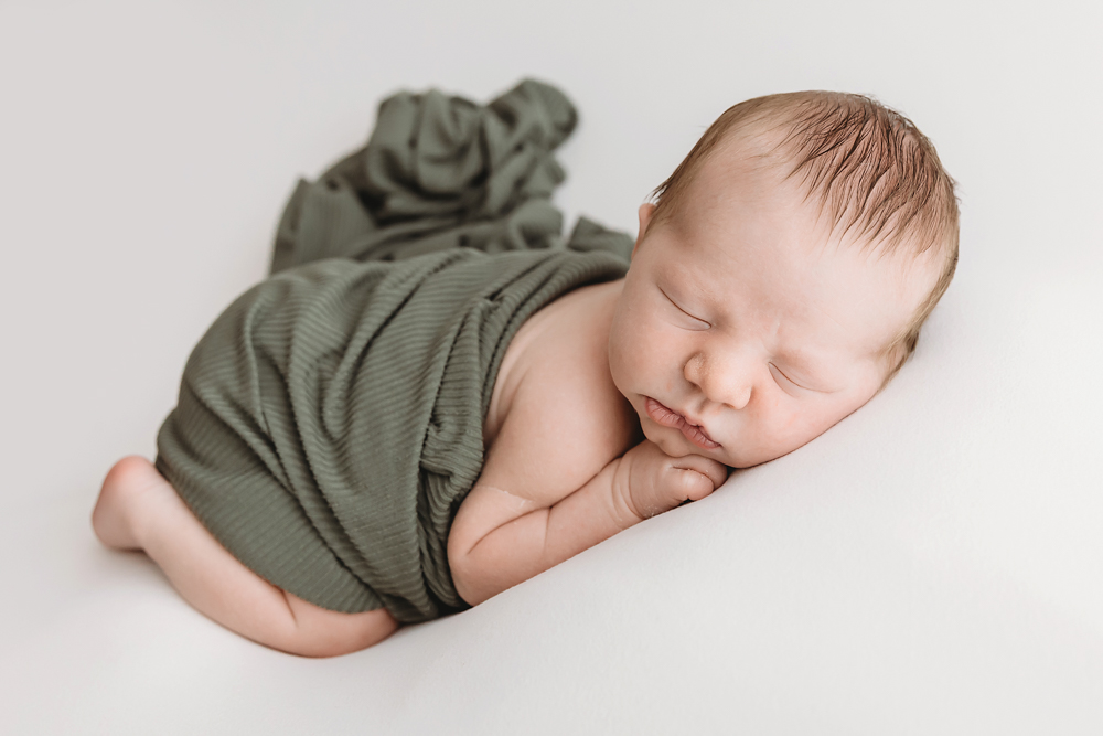 Sleeping newborn baby wrapped in olive green textured blanket on white backdrop - Reflection Images by Tracy Rowell