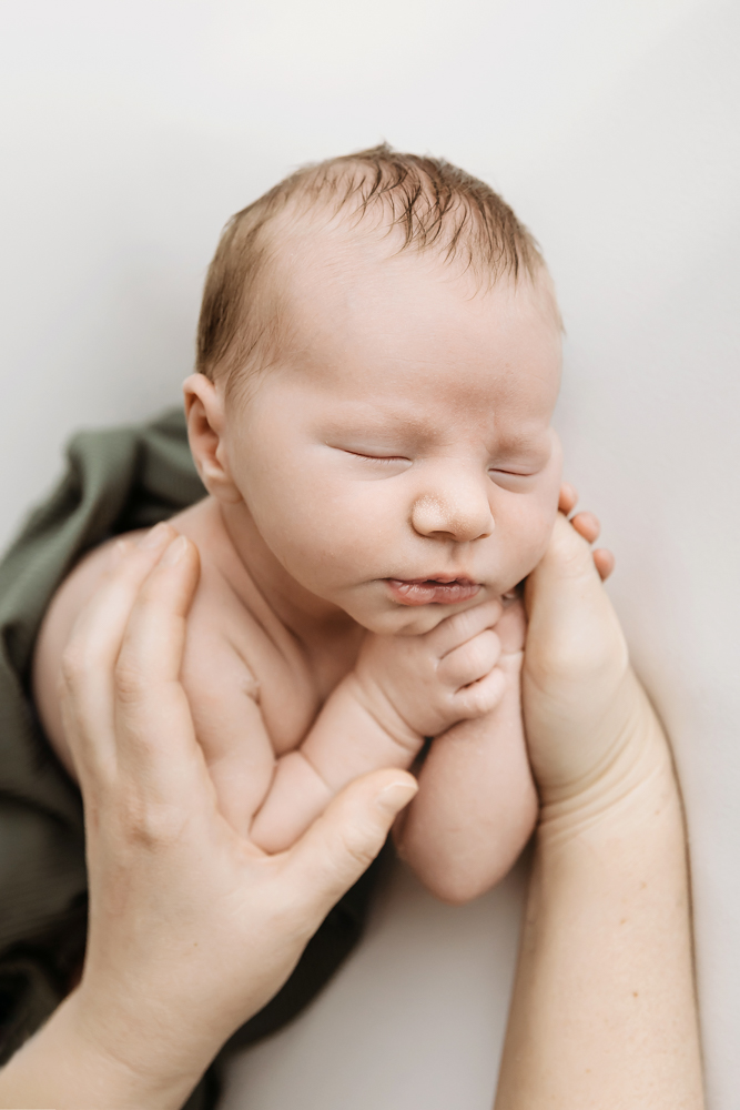 Sleeping baby cradled in gentle hands on soft green fabric, peaceful newborn pictures with warm natural lighting