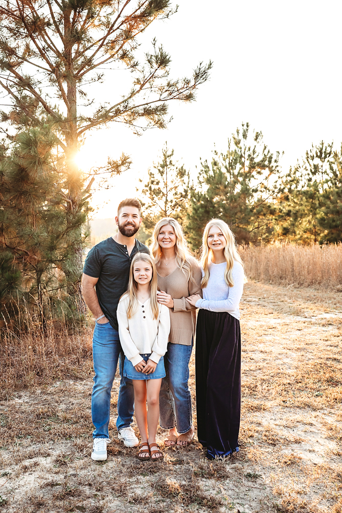 Family of four posing outdoors at golden hour with warm sunlight filtering through trees, professional photography studio