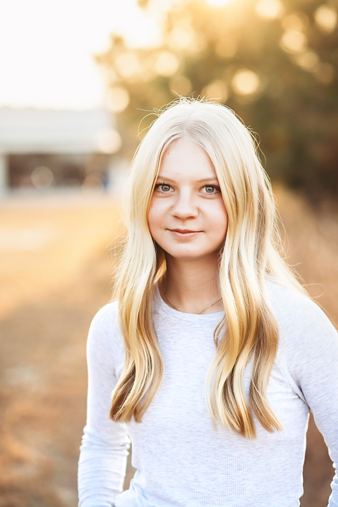 Teen girl with long blonde hair in white sweater, golden hour portrait with soft bokeh background by florence sc photographer