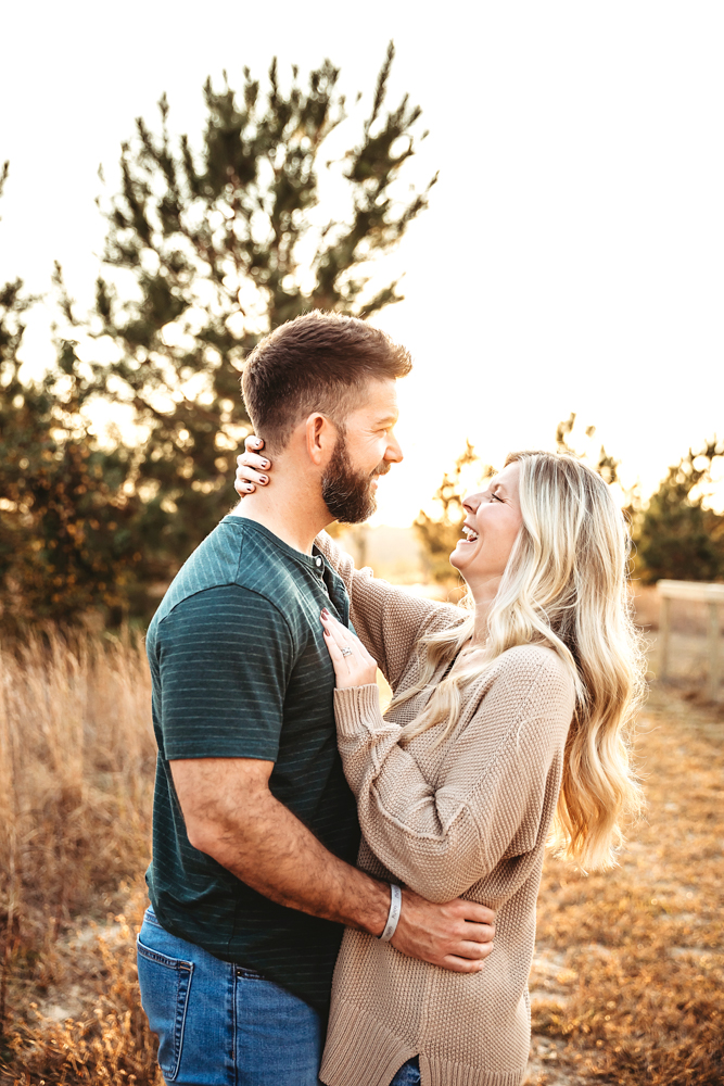 Couple embracing in golden sunset light, man in teal shirt, blonde woman in beige sweater, professional photographer near me