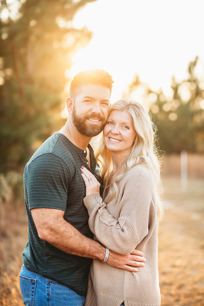 Smiling couple embracing outdoors in warm golden hour light, man in dark henley, woman in beige sweater, professional photography