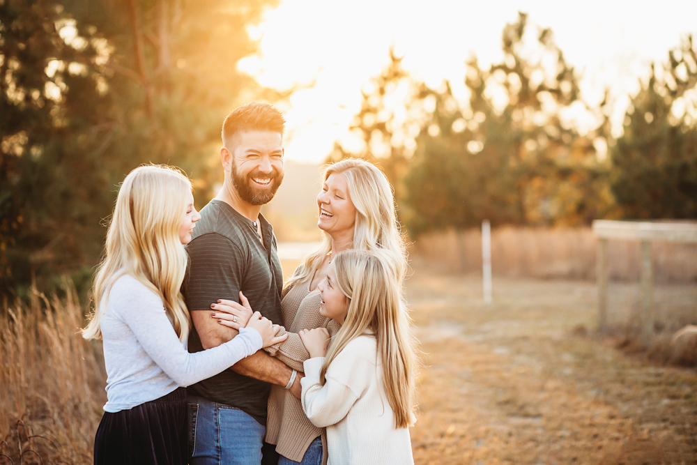 Professional fall family pictures of laughing family in golden sunset light, wearing neutral sweaters and white tops outdoors