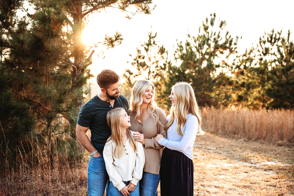 Laughing family of four in natural outdoor setting with golden sunset light, professional photography portrait session