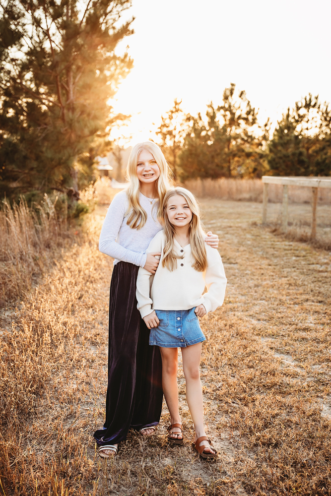 Smiling mother and daughter embracing in golden sunset light for fall family photography, wearing white tops in rustic field