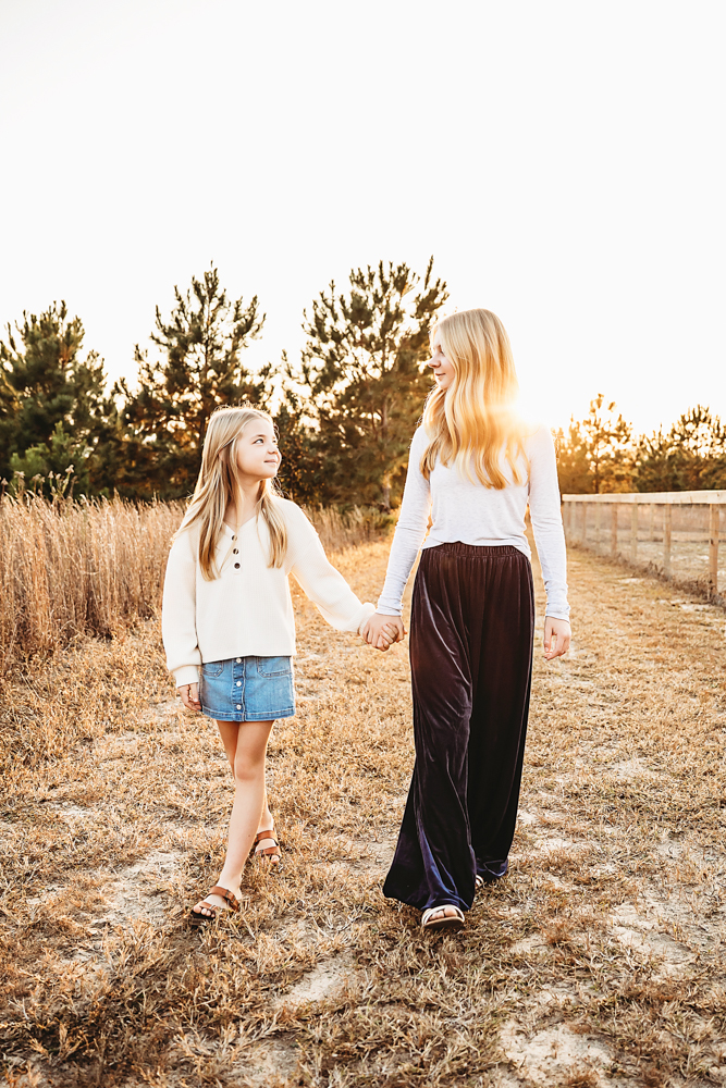 Teen and adult holding hands in golden field at sunset, white tops, denim skirt and dark pants, florence sc fall family photographer