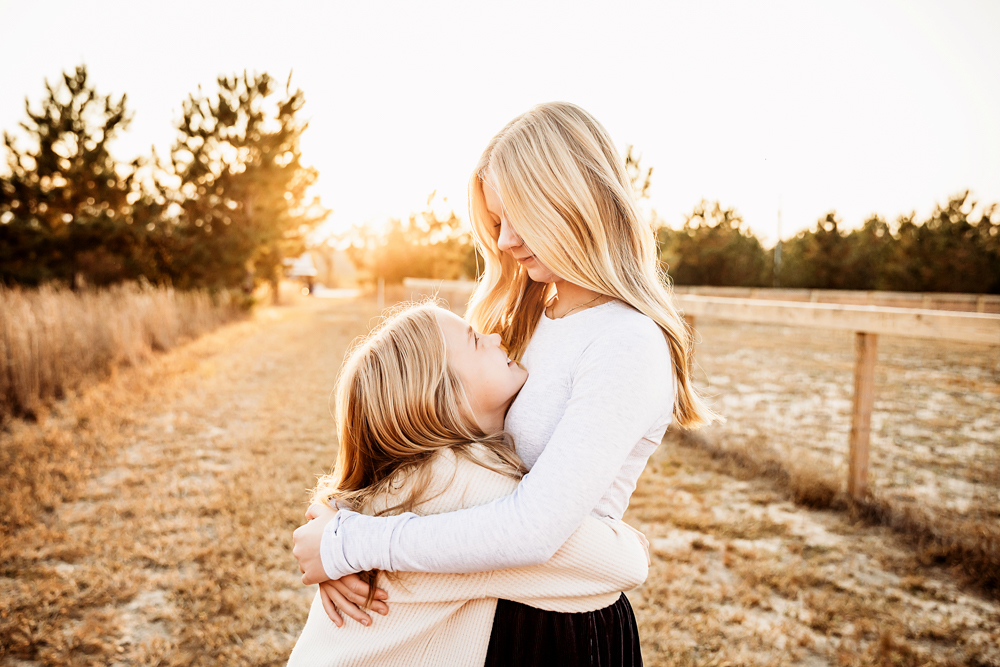 Mother and child embrace in golden sunset field, wearing white tops, warm lighting, professional photography studio near me