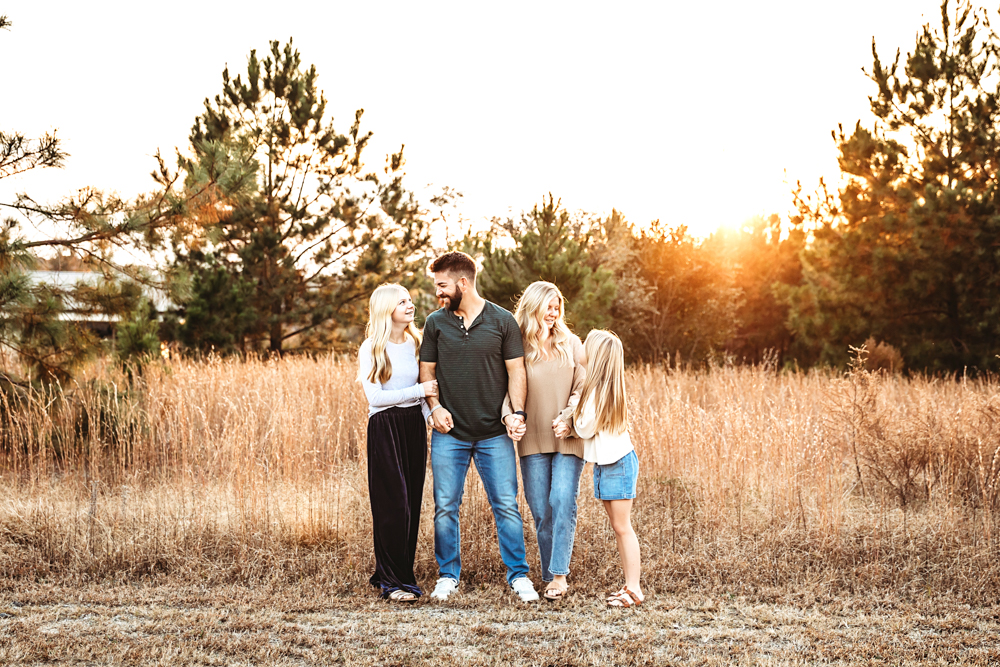 Family of four in golden field at sunset, professional photography studio, parents and two children in casual clothing