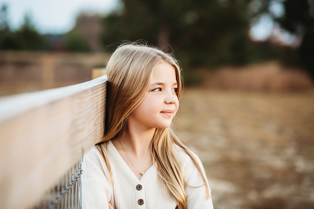 Teen girl with long blonde hair in cream cardigan looking off-camera on wooden bridge, fall family photographer session