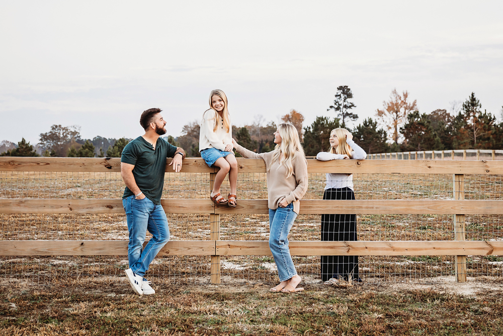 Family of four at wooden farm fence, dad in green shirt, mom in beige top, kids in casual wear - Reflection Images by Tracy Rowell