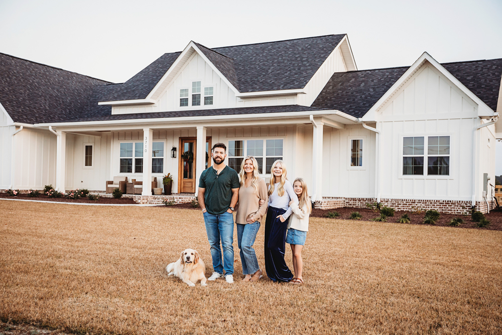 Family of four with golden retriever standing in front of white farmhouse home, photographed by Tracy Rowell