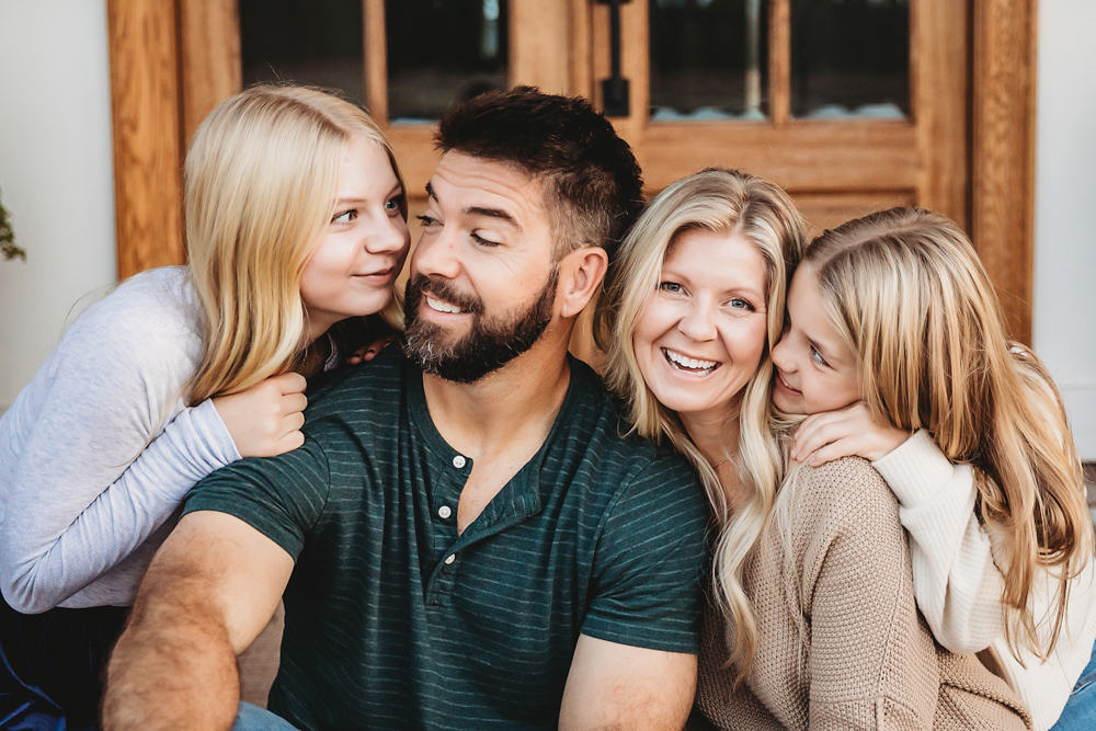 Happy family of four embracing and laughing together indoors, professional photography studio near me captures warm moment