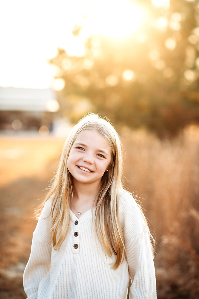 Smiling child in cream ribbed sweater with golden sunset lighting and autumn bokeh by fall family photographer