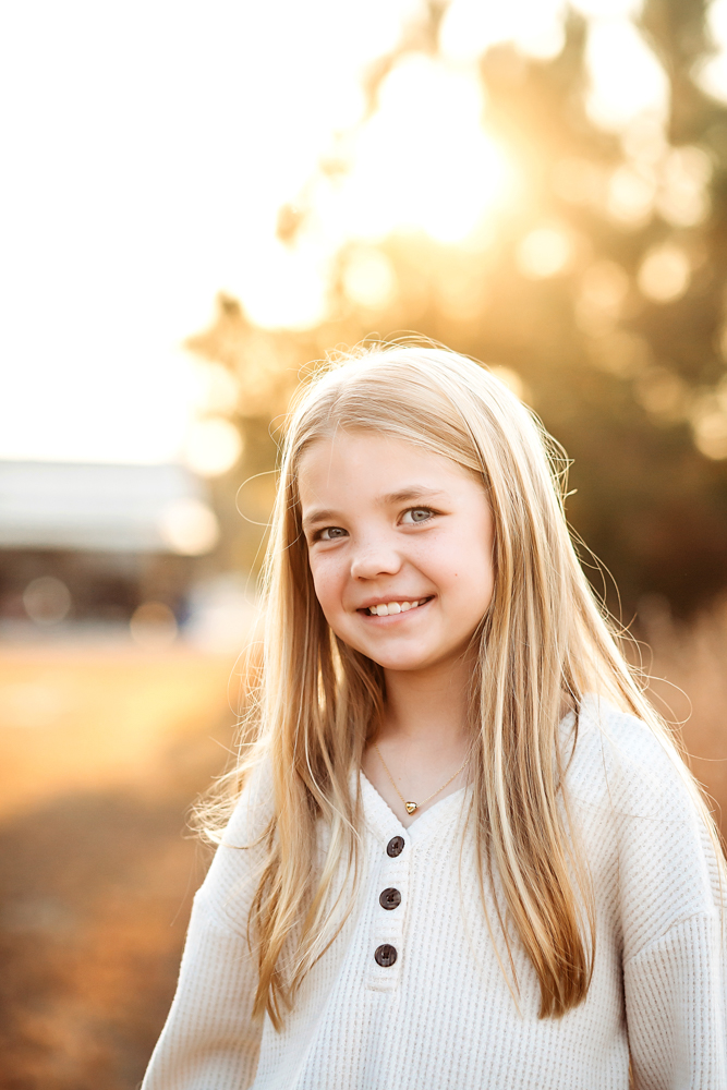 Smiling child with long blonde hair in white ribbed sweater, golden sunset backlight, Tracy Rowell portrait photography