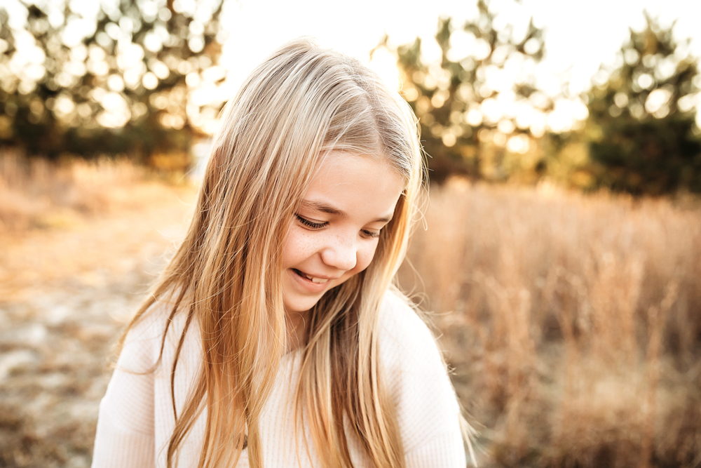 Smiling blonde child in cream sweater during golden hour fall family photos with warm autumn field backdrop