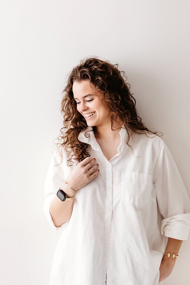 Smiling adult with curly brown hair in white button-up shirt against cream backdrop, florence sc newborn photographer portrait