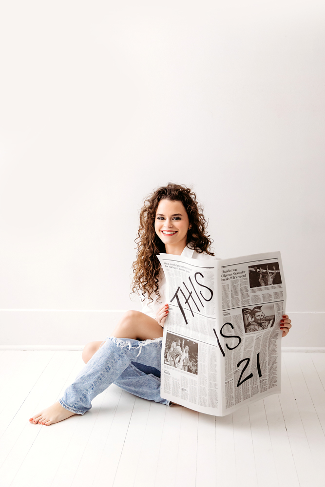 Smiling young woman with curly brown hair holding newspaper reading 