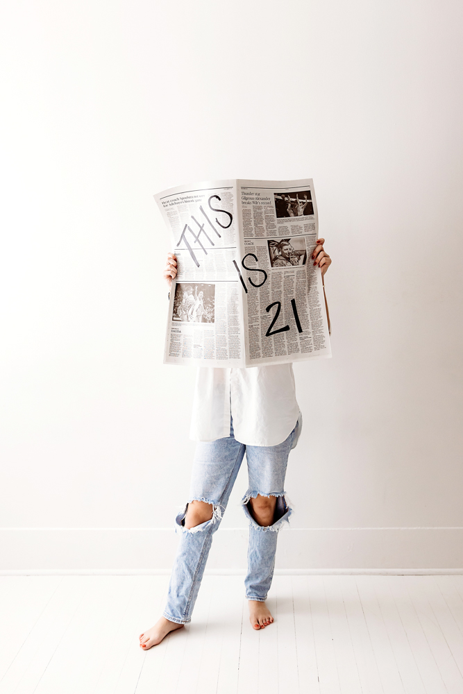 Teen holding newspaper hiding face, wearing white shirt and ripped jeans, professional photography studio near me bright lighting