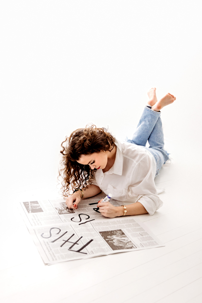 Teen with curly hair writing in white shirt and jeans on white backdrop, professional photography near me studio portrait
