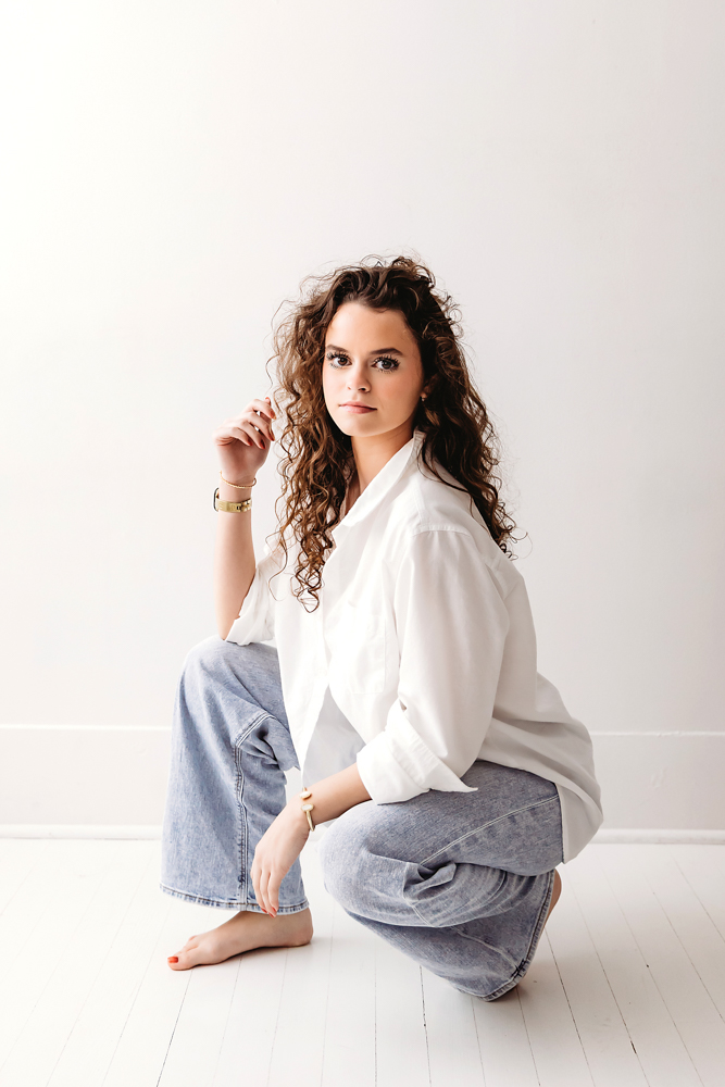 Young woman with curly hair in white shirt and jeans sitting on white floor, soft natural lighting - Reflection Images by Tracy Rowell