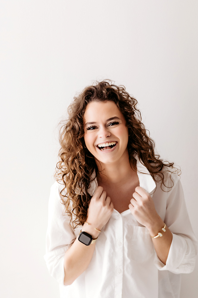 Young adult woman laughing joyfully in white shirt against cream backdrop in professional photography studio