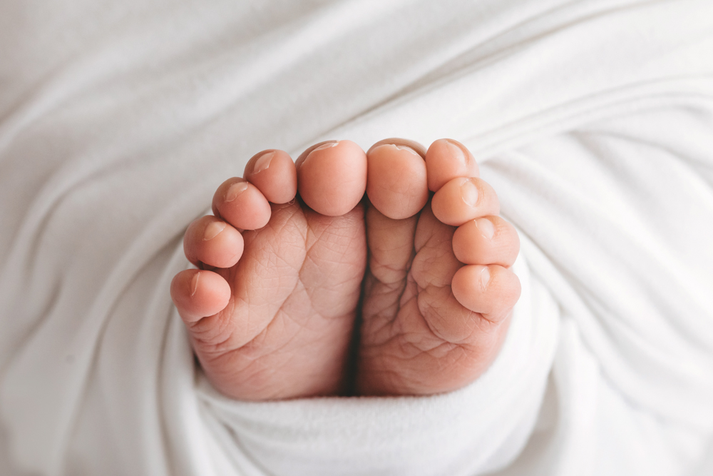 Tiny baby feet on soft white blanket for newborn photography session with gentle natural lighting and cream backdrop