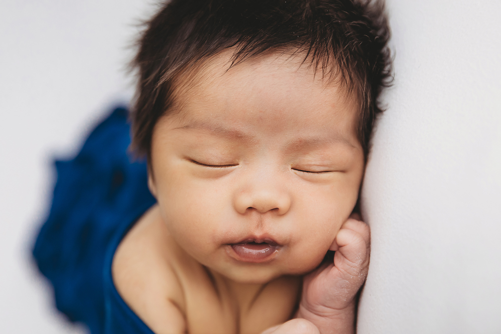 Peaceful sleeping baby with dark hair resting on adult hand in soft natural lighting for newborn pictures session