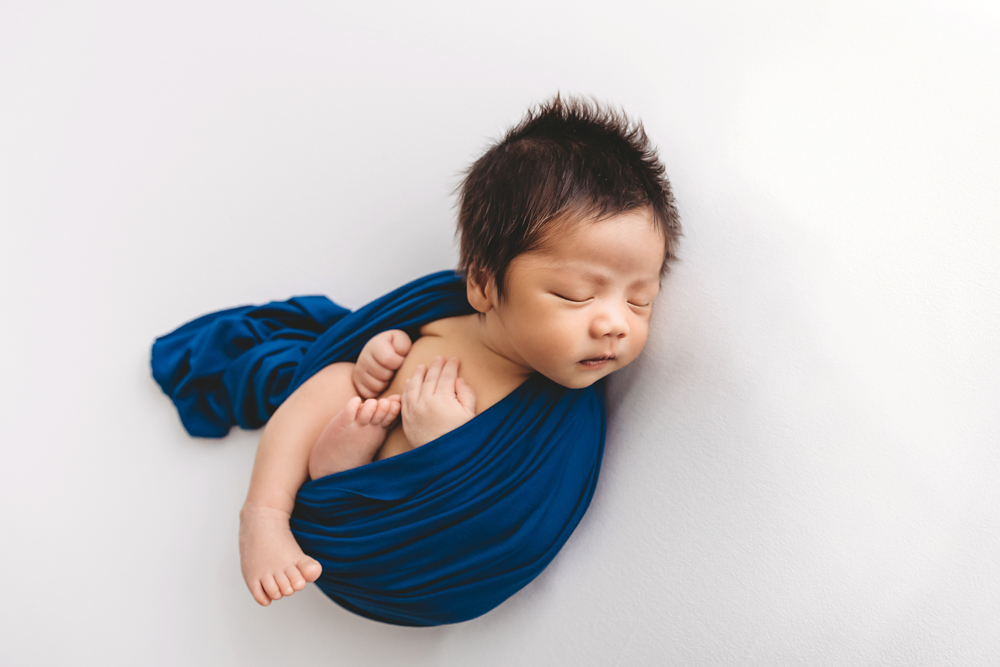 Sleeping newborn baby wrapped in blue fabric on white backdrop, soft lighting - florence sc photographer