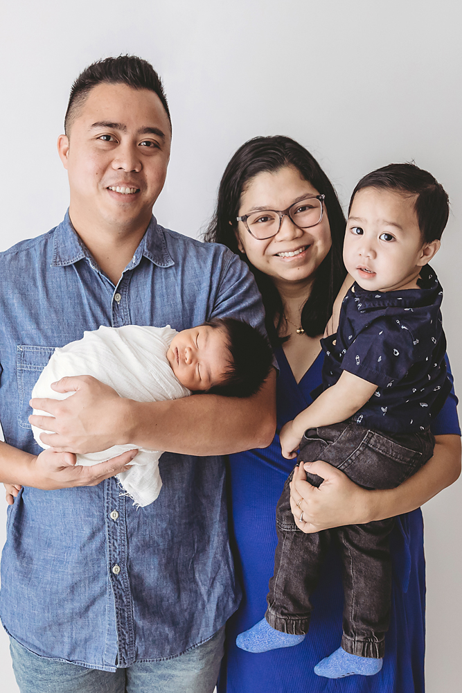 Happy family of four with newborn baby in white blanket, toddler in navy shirt, florence sc newborn photographer portrait