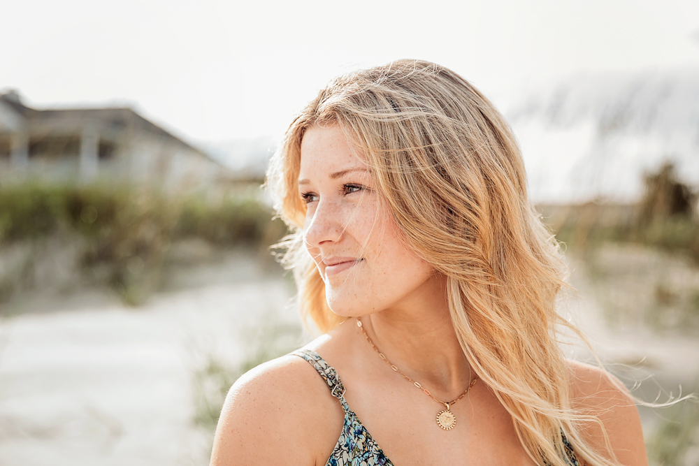 Young blonde woman in floral dress and gold necklace smiling at Pawleys Island SC beach family session.