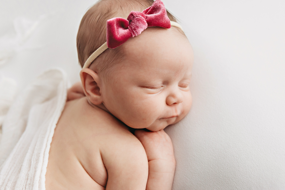 Newborn Gracyn wearing a velvet rose bow by Florence SC newborn photographer Tracy Rowell on a soft white muslin wrap.