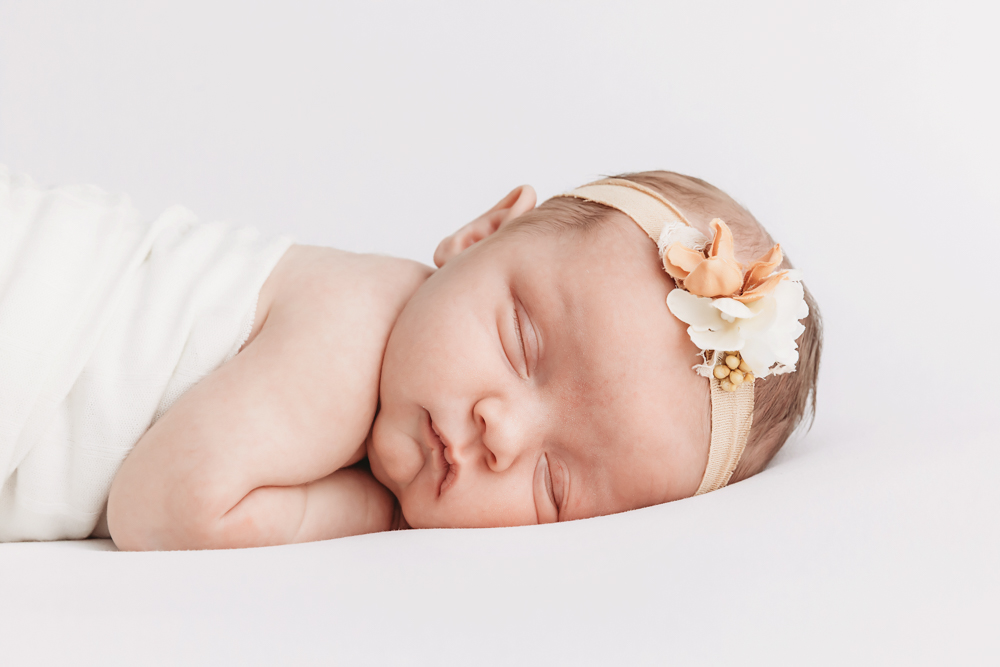 Sleeping newborn girl by Florence SC photographer Tracy Rowell wearing a peach floral headband and ivory knit wrap.