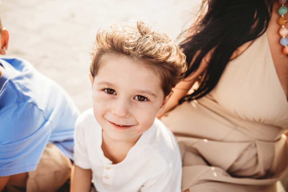 Smiling boy in white henley shirt at Pawleys Island SC beach with family, captured by beach family photographer.