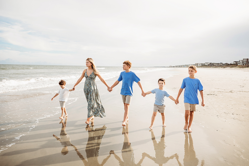 Mother and sons in blue and sage green floral dress holding hands walking on Pawleys Island SC beach for family photos.