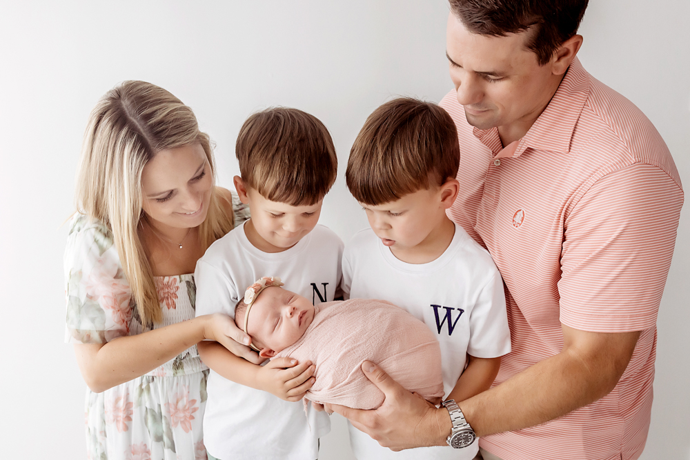 Family portrait by Reflection Images in Florence SC showing parents and brothers cradling a newborn in a dusty rose wrap.