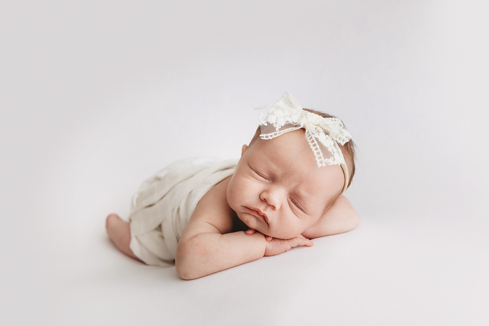 Sleeping newborn girl with ivory lace headband on cream backdrop by Florence SC newborn photographer Tracy Rowell.