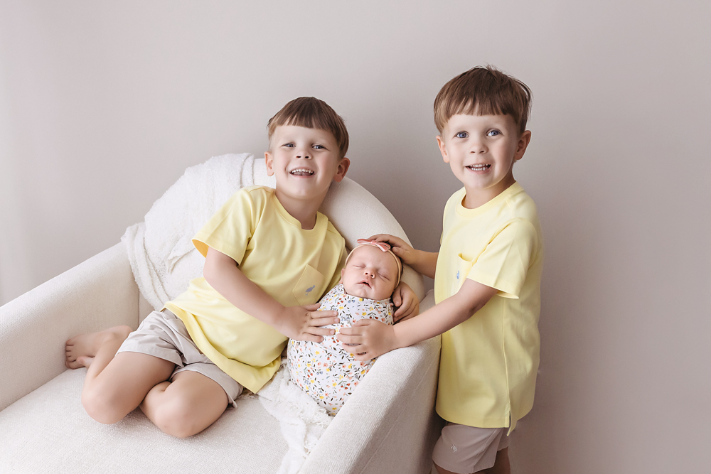 twin big brothers in lemon yellow tees smile with their newborn sister in a floral swaddle by Reflection Images, Florence SC.sibing pose