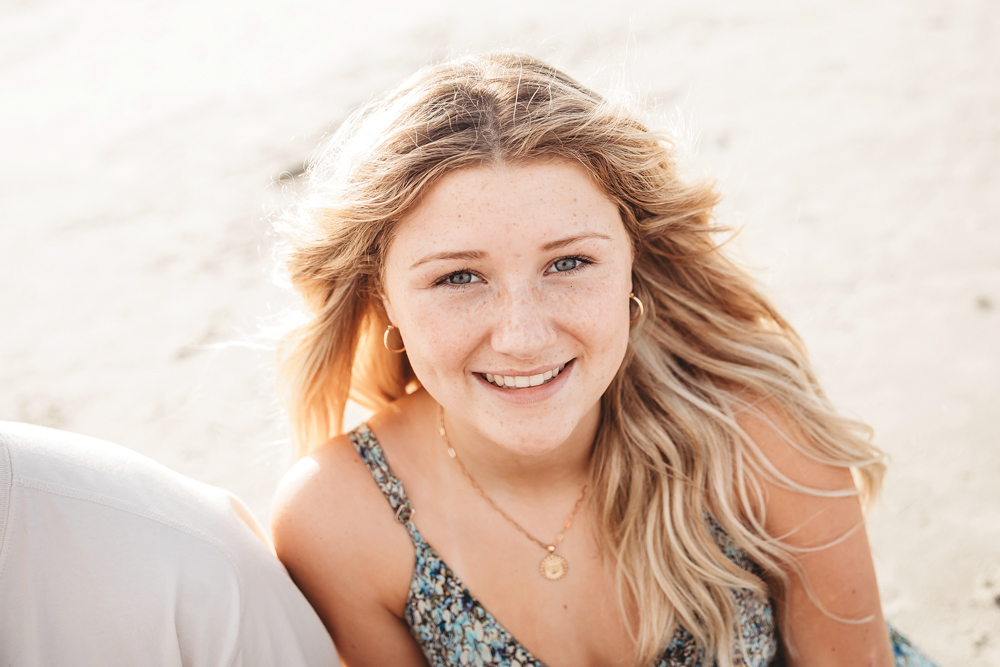 Smiling blonde girl with freckles in blue floral dress at Pawleys Island SC during a beach family session.