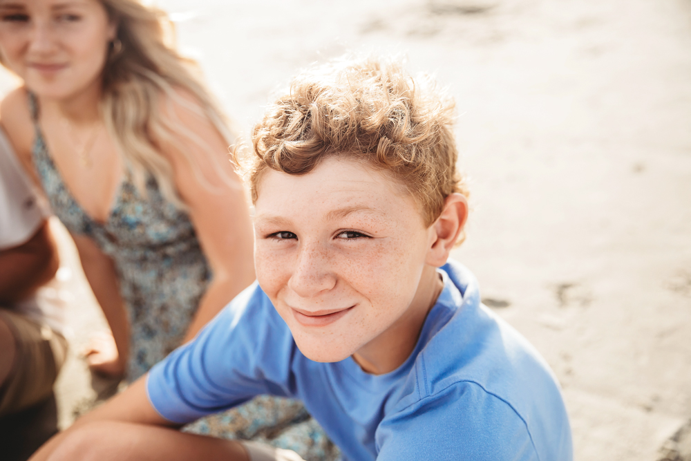 Curly-haired boy in cornflower blue shirt at Pawleys Island SC beach, family photography by Reflection Images.