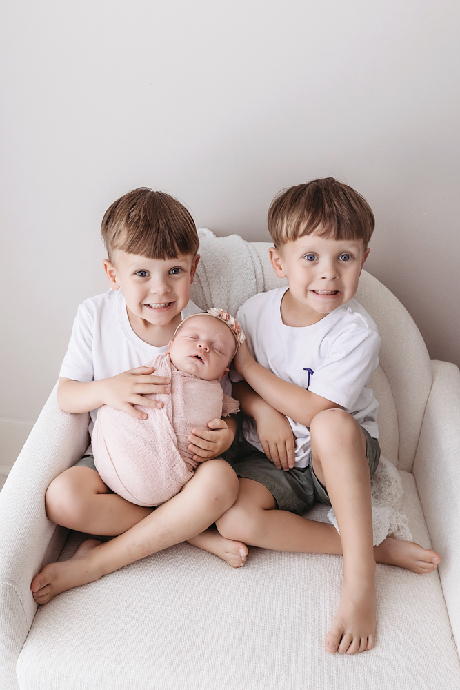 Newborn girl in blush muslin wrap with floral headband held by two brothers, Florence SC newborn photography by Tracy Rowell