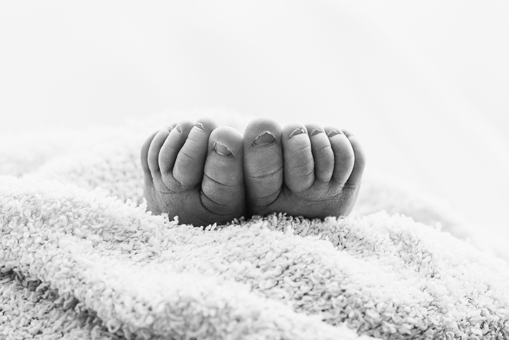 Black and white newborn photography by Reflection Images in Florence SC, showing tiny baby feet nestled in a soft blanket.