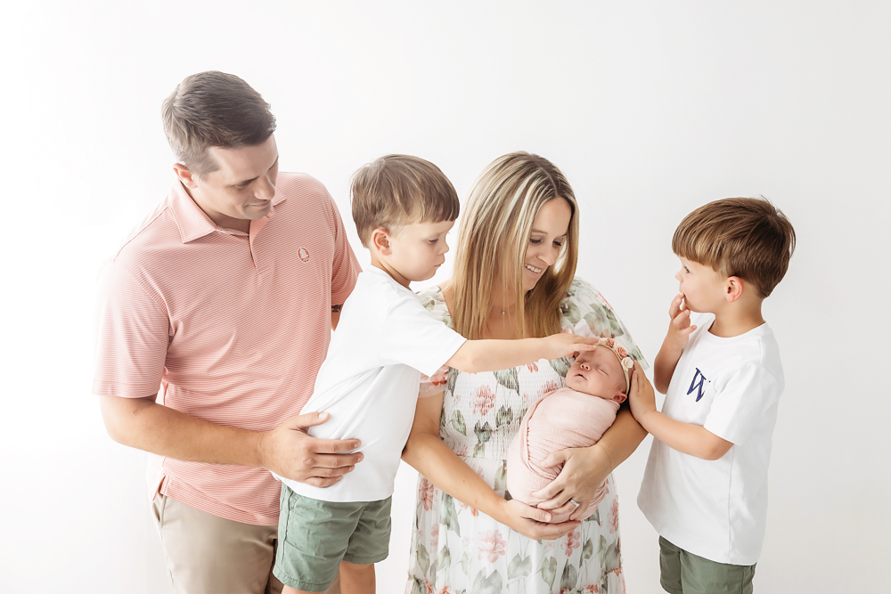 Family portrait by Reflection Images in Florence SC. Parents and brothers touch a newborn in a blush knit wrap.