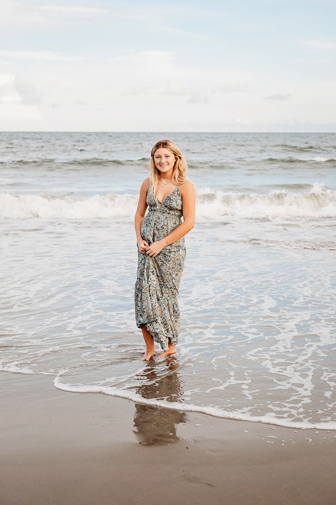 Smiling teen in sage floral maxi dress standing in surf for beach family photography at Pawleys Island SC.