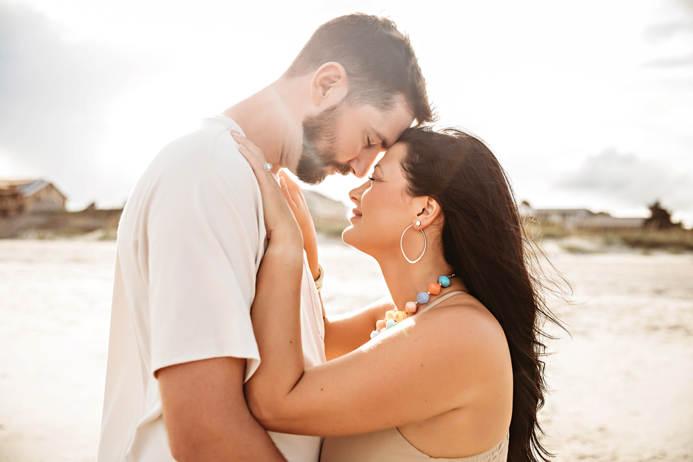 Couple touching foreheads in color beach family photos at Pawleys Island SC wearing taupe shirts and turquoise jewelry.