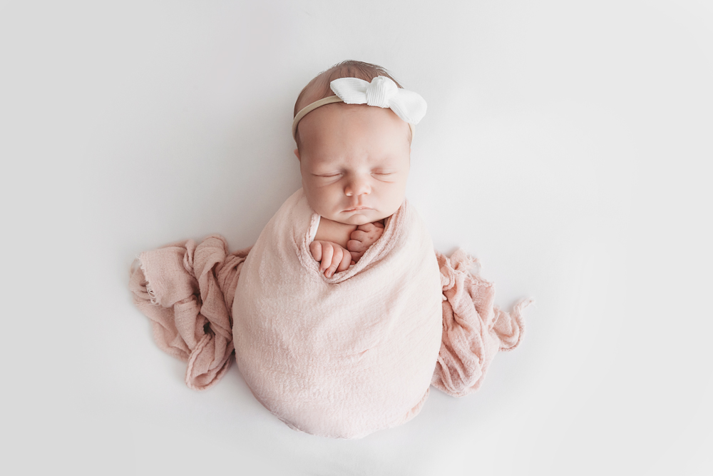Sleeping newborn in dusty rose knit wrap with white bow headband by Reflection Images Florence SC newborn photographer.