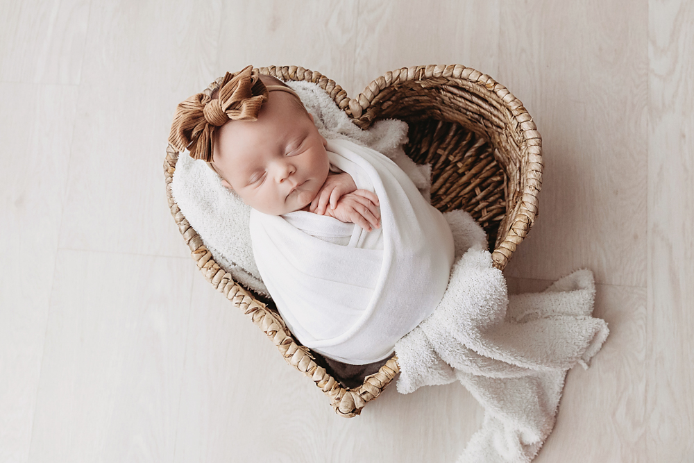 Gracyn in heart wicker basket, ivory muslin wrap, tan velvet bow by Tracy Rowell, Florence SC newborn photographer.