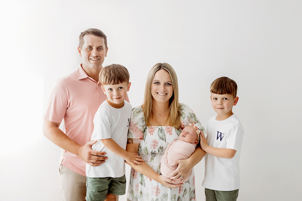 Florence SC newborn family session by Tracy Rowell showing parents and two boys holding baby in a dusty rose knit wrap.