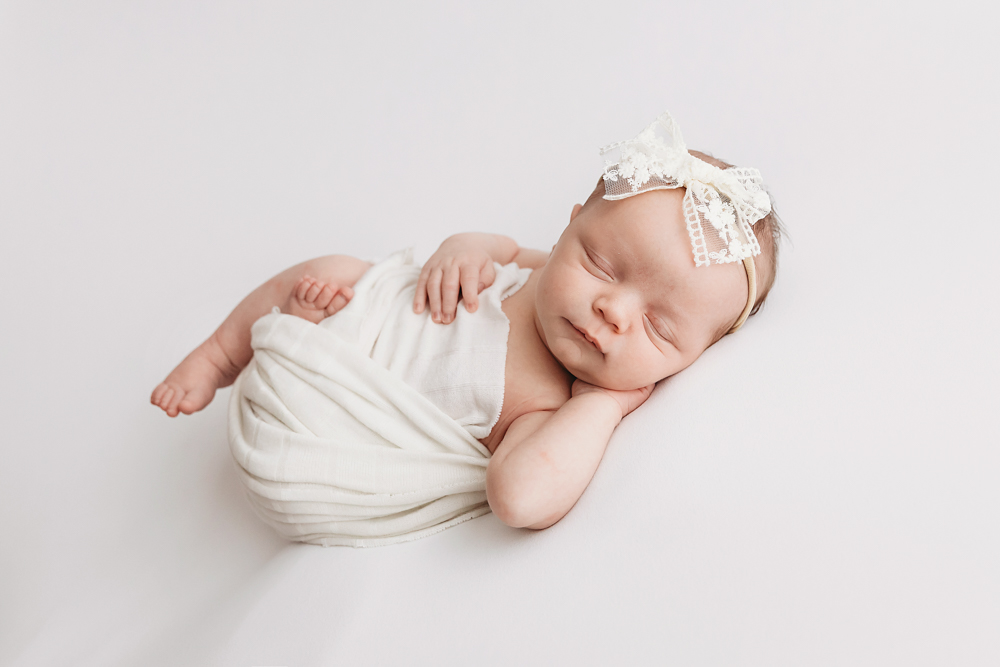 Sleeping newborn girl in ivory knit wrap with lace bow by Tracy Rowell, professional newborn photographer in Florence SC.