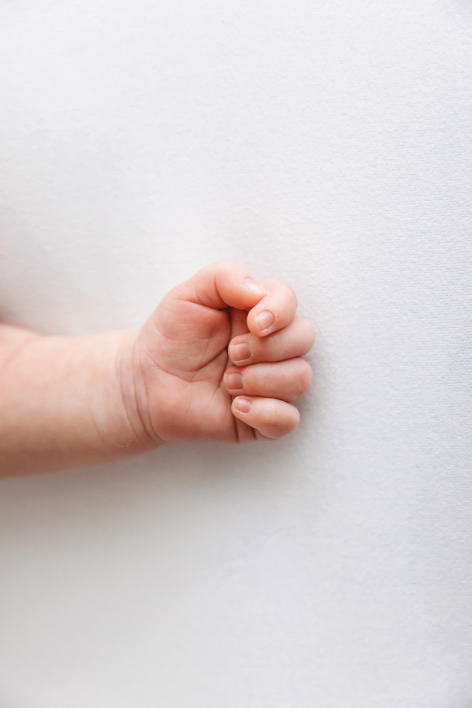 Newborn baby hand curled in a fist on ivory fabric by Florence SC newborn photographer Reflection Images by Tracy Rowell.